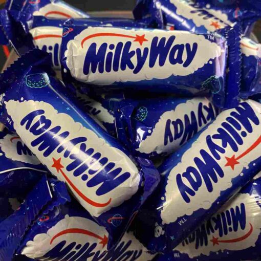 MilkyWay chokoladebar delvist åbnet for at vise blødt nougat og cremet flødefyld omgivet af mælkechokolade på mørk baggrund.